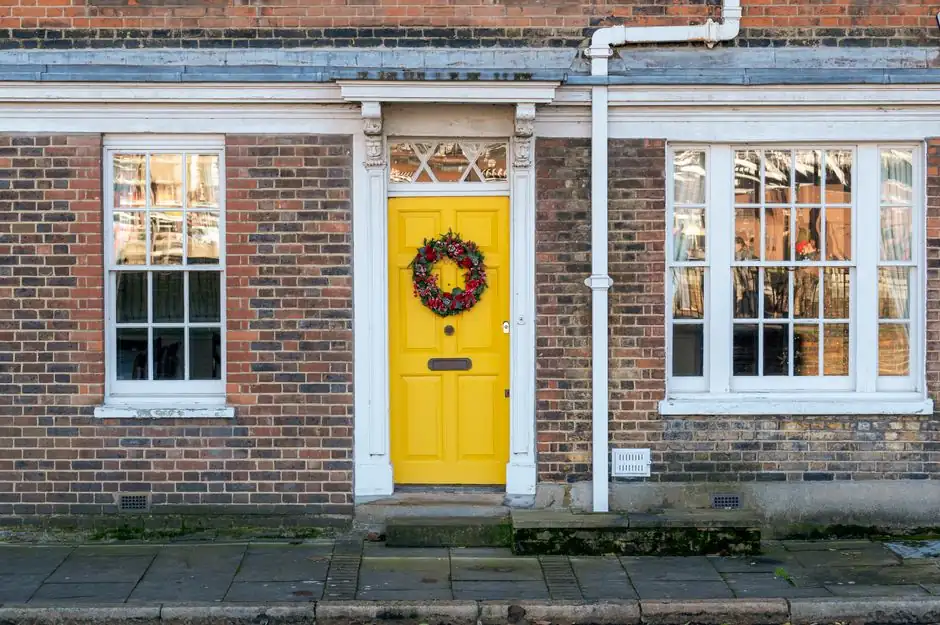 Charming yellow door adorned with a festive wreath, set in a classic brick facade on a quiet street.